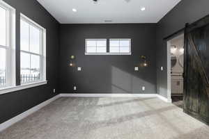 Empty room featuring a barn door and light carpet