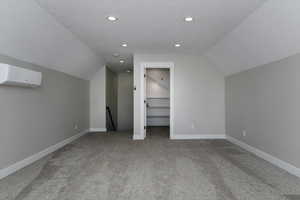 Additional living space featuring carpet floors, a textured ceiling, a wall unit AC, and vaulted ceiling