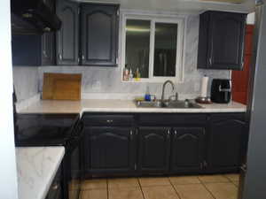 Kitchen featuring sink, black electric range, stainless steel fridge, light tile patterned floors, and extractor fan