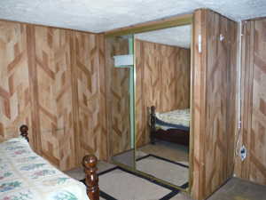 Bedroom featuring wood walls, a closet, and a textured ceiling