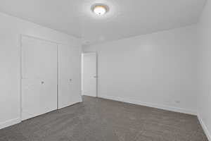 Unfurnished bedroom with a textured ceiling, dark carpet, and a closet