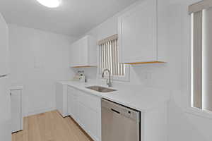 Kitchen with stainless steel dishwasher, sink, light hardwood / wood-style flooring, white cabinets, and plenty of natural light