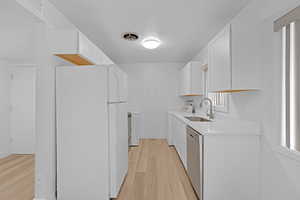 Kitchen featuring dishwasher, sink, white refrigerator, light hardwood / wood-style floors, and white cabinets