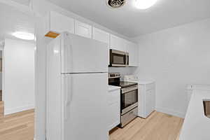 Kitchen featuring white cabinets, light wood-type flooring, stainless steel appliances, and washer / clothes dryer