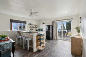 Kitchen featuring black refrigerator, ceiling fan, white cabinetry, kitchen peninsula, and a breakfast bar area