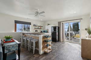 Kitchen with black fridge, kitchen peninsula, ceiling fan, a kitchen bar, and white cabinetry