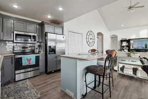 Kitchen with appliances with stainless steel finishes, tasteful backsplash, a breakfast bar, gray cabinets, and a kitchen island