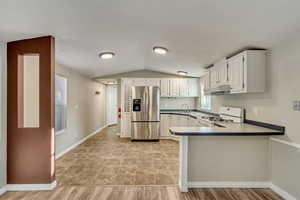 Kitchen featuring white cabinets, white range, stainless steel fridge with ice dispenser, and vaulted ceiling