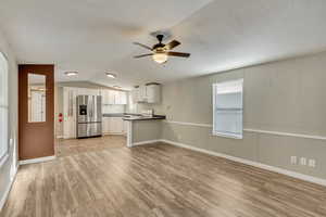 Kitchen with lofted ceiling, white cabinets, light hardwood / wood-style flooring, ceiling fan, and stainless steel fridge