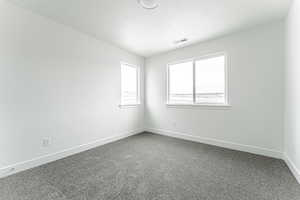 Empty room featuring dark carpet, a textured ceiling, visible vents, and baseboards