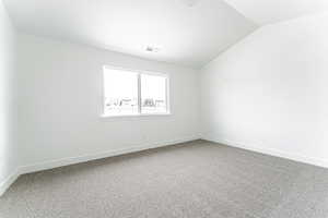Empty room with baseboards, visible vents, carpet flooring, and vaulted ceiling