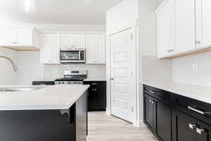 Kitchen with appliances with stainless steel finishes, white cabinetry, light countertops, and a sink