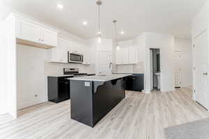 Kitchen with light wood finished floors, a sink, stainless steel appliances, dark cabinetry, and a breakfast bar area