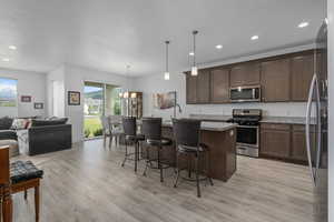 Kitchen featuring pendant lighting, a kitchen breakfast bar, an island with sink, light stone counters, and stainless steel appliances