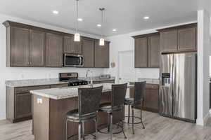 Kitchen with a center island with sink, light stone countertops, decorative light fixtures, dark brown cabinetry, and stainless steel appliances