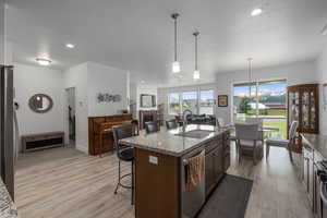 Kitchen featuring stainless steel appliances, sink, dark stone countertops, hanging light fixtures, and an island with sink