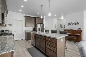 Kitchen featuring light stone countertops, appliances with stainless steel finishes, a kitchen island with sink, sink, and pendant lighting