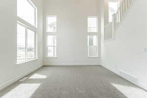 Carpeted spare room featuring baseboards, visible vents, stairs, and a towering ceiling