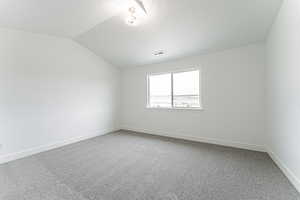 Unfurnished room with a textured ceiling, visible vents, baseboards, vaulted ceiling, and light carpet
