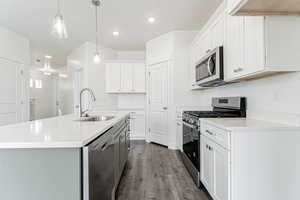 Kitchen featuring hanging light fixtures, appliances with stainless steel finishes, light countertops, a sink, and dark wood-type flooring
