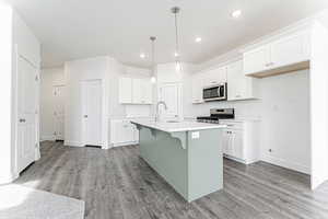 Kitchen with light wood finished floors, a sink, a breakfast bar area, white cabinets, and appliances with stainless steel finishes