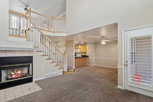 Unfurnished living room with carpet, a high ceiling, ceiling fan, ornamental molding, and a tiled fireplace