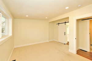 Unfurnished room featuring a textured ceiling, a barn door, and light carpet