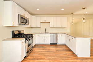 Kitchen featuring sink, kitchen peninsula, decorative light fixtures, white cabinets, and appliances with stainless steel finishes