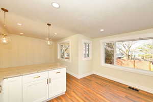 Kitchen featuring white cabinetry, light stone countertops, pendant lighting, and light hardwood / wood-style floors