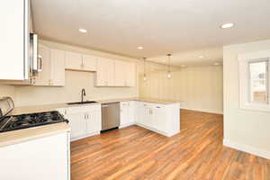 Kitchen featuring white cabinetry, dishwasher, sink, stove, and decorative light fixtures