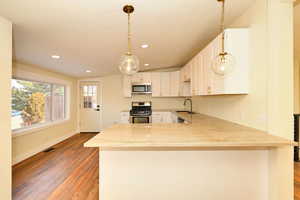 Kitchen featuring dark wood-type flooring, white cabinets, sink, appliances with stainless steel finishes, and kitchen peninsula