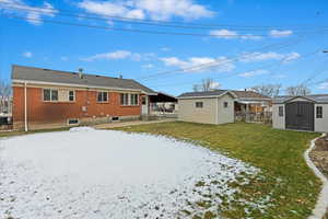 Snow covered back of property with central AC, a storage unit, and a lawn