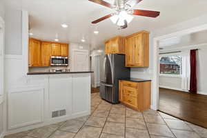 Kitchen featuring dark stone counters, ceiling fan, light tile patterned floors, appliances with stainless steel finishes, and kitchen peninsula