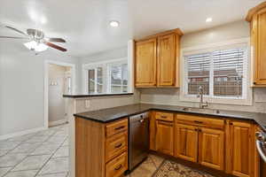 Kitchen featuring dishwasher, sink, ceiling fan, dark stone countertops, and kitchen peninsula