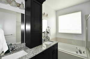 Bathroom featuring vanity, a relaxing tiled tub, and a wealth of natural light