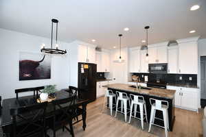 Kitchen with tasteful backsplash, black appliances, dark stone countertops, white cabinetry, and an island with sink