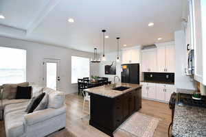 Kitchen with black appliances, white cabinets, sink, light hardwood / wood-style flooring, and an island with sink