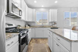 Kitchen with light stone countertops, white cabinetry, sink, light hardwood / wood-style flooring, and appliances with stainless steel finishes