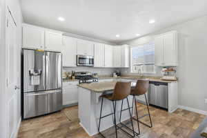 Kitchen featuring stainless steel appliances, a kitchen island, hardwood / wood-style floors, a breakfast bar, and white cabinets