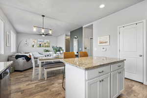 Kitchen featuring white cabinetry, dishwasher, decorative light fixtures, a breakfast bar, and a kitchen island