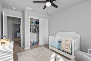 Bedroom with ceiling fan, a crib, light carpet, and a closet