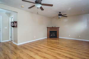 Unfurnished living room featuring ceiling fan, a textured ceiling, and light wood-type flooring