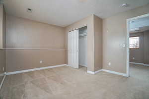 Unfurnished bedroom featuring light carpet, a closet, and a textured ceiling