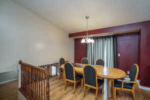 Dining room featuring wood-type flooring, vaulted ceiling, and a notable chandelier