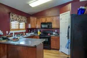 Kitchen featuring sink, kitchen peninsula, vaulted ceiling, black appliances, and light wood-type flooring