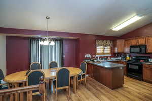 Kitchen with kitchen peninsula, light wood-type flooring, vaulted ceiling, black appliances, and pendant lighting