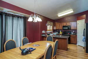 Kitchen featuring hanging light fixtures, light hardwood / wood-style flooring, a notable chandelier, lofted ceiling, and black appliances