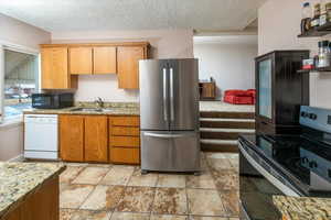 Kitchen featuring light stone countertops, a textured ceiling, stainless steel appliances, and sink