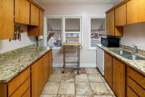 Kitchen with white dishwasher, light stone counters, and sink