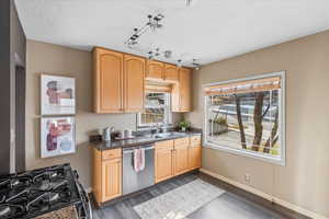 Kitchen featuring black gas stove, sink, stainless steel dishwasher, dark hardwood / wood-style floors, and light brown cabinetry